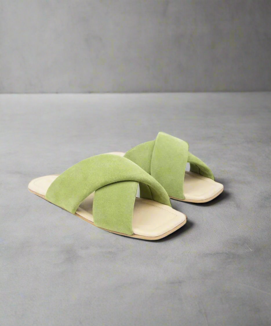 Green sandals with criss-cross straps on a grey background