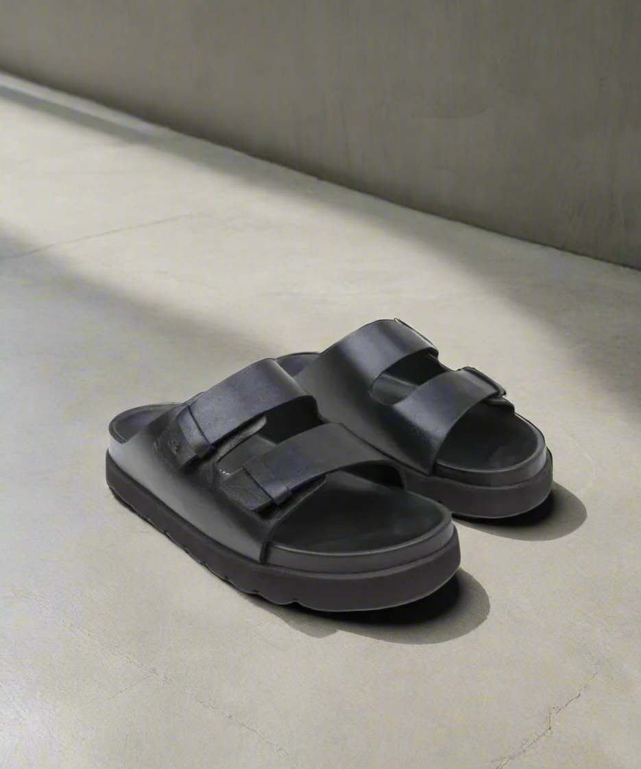 Black sandals with double straps on a gray background