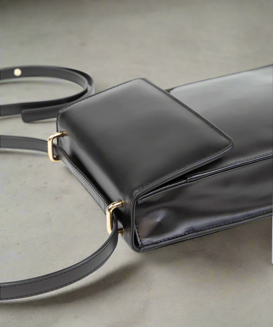 Black handbag with gold hardware on a light gray background