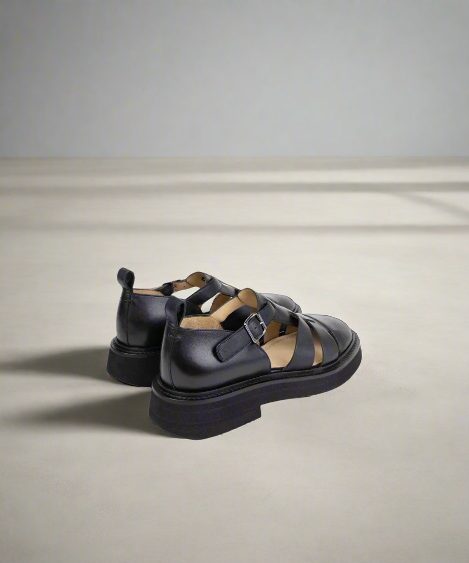 Black sandals with strap details on a gray background