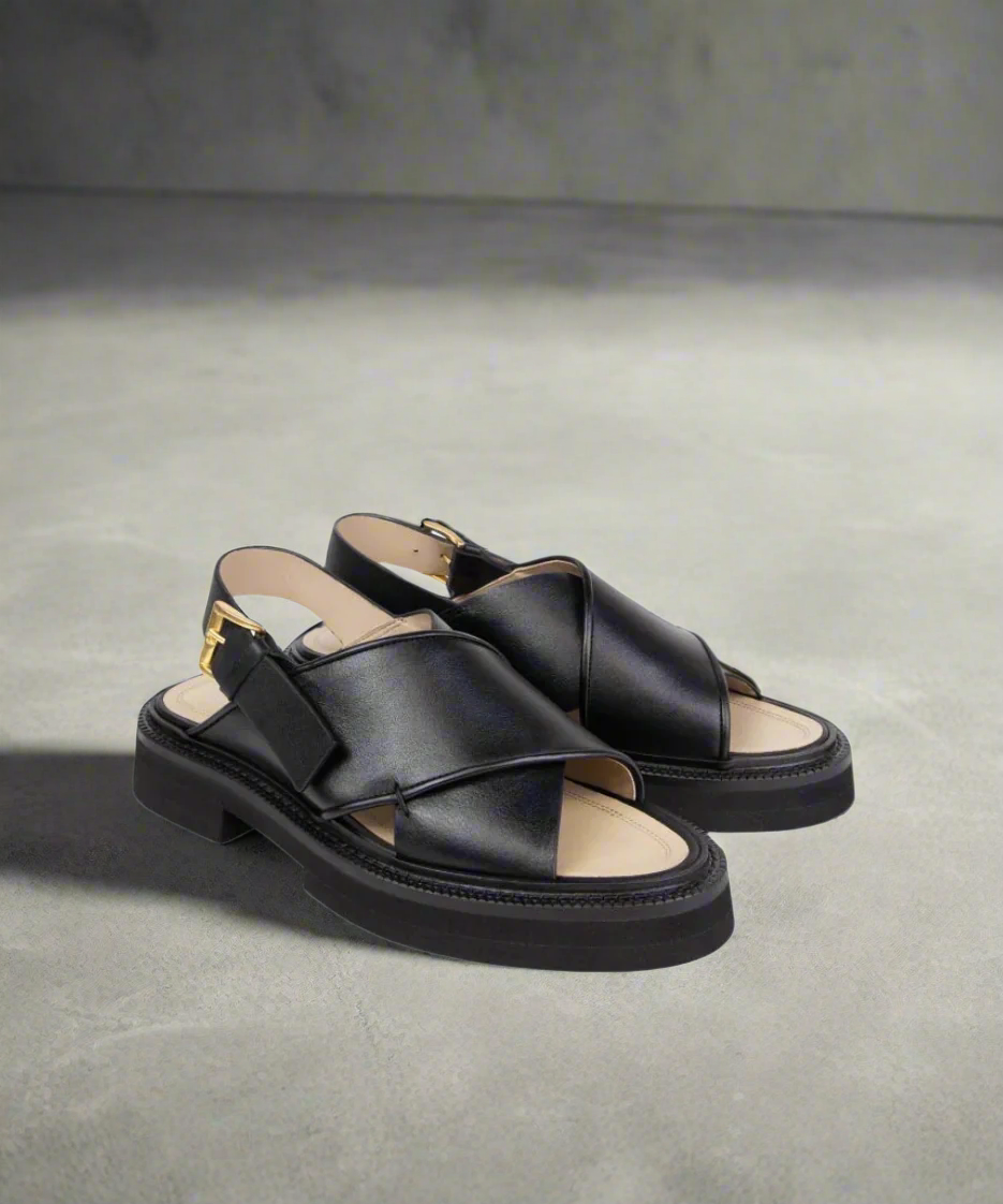 Black sandals with criss-cross straps on a gray background