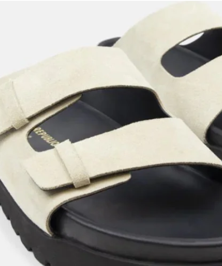 Black and beige sandals with a visible brand logo on a gray background
