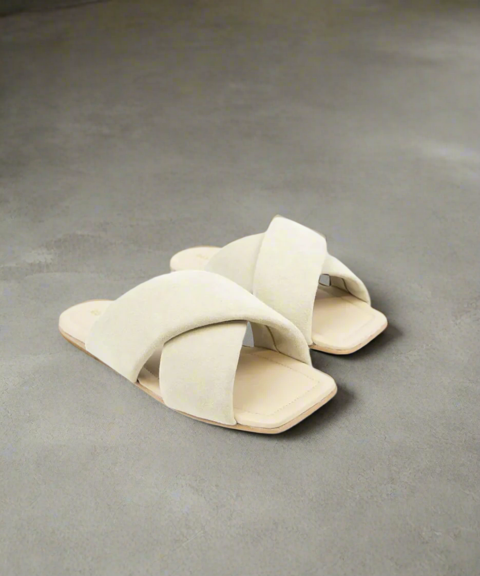 Pair of beige sandals with criss-cross straps on a gray background