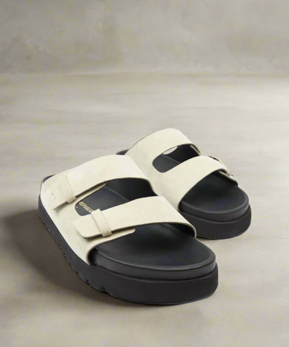 Beige sandals with black soles on a gray background