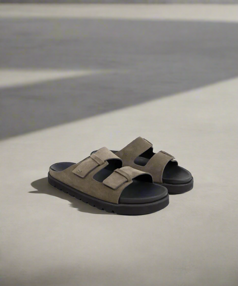 Pair of brown sandals with black soles on a light gray background