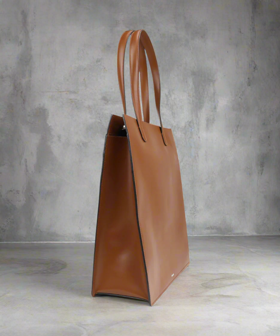 Brown leather tote bag against a gray concrete wall
