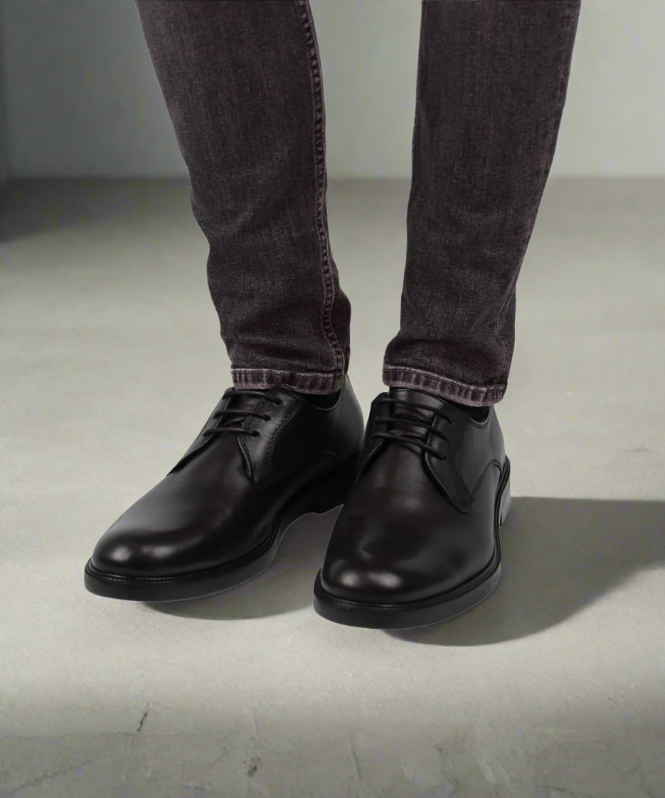 Black leather shoes worn with dark jeans on a gray background