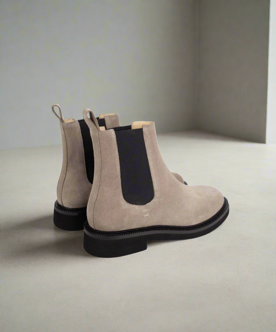 Pair of beige Chelsea boots with black soles on a gray background