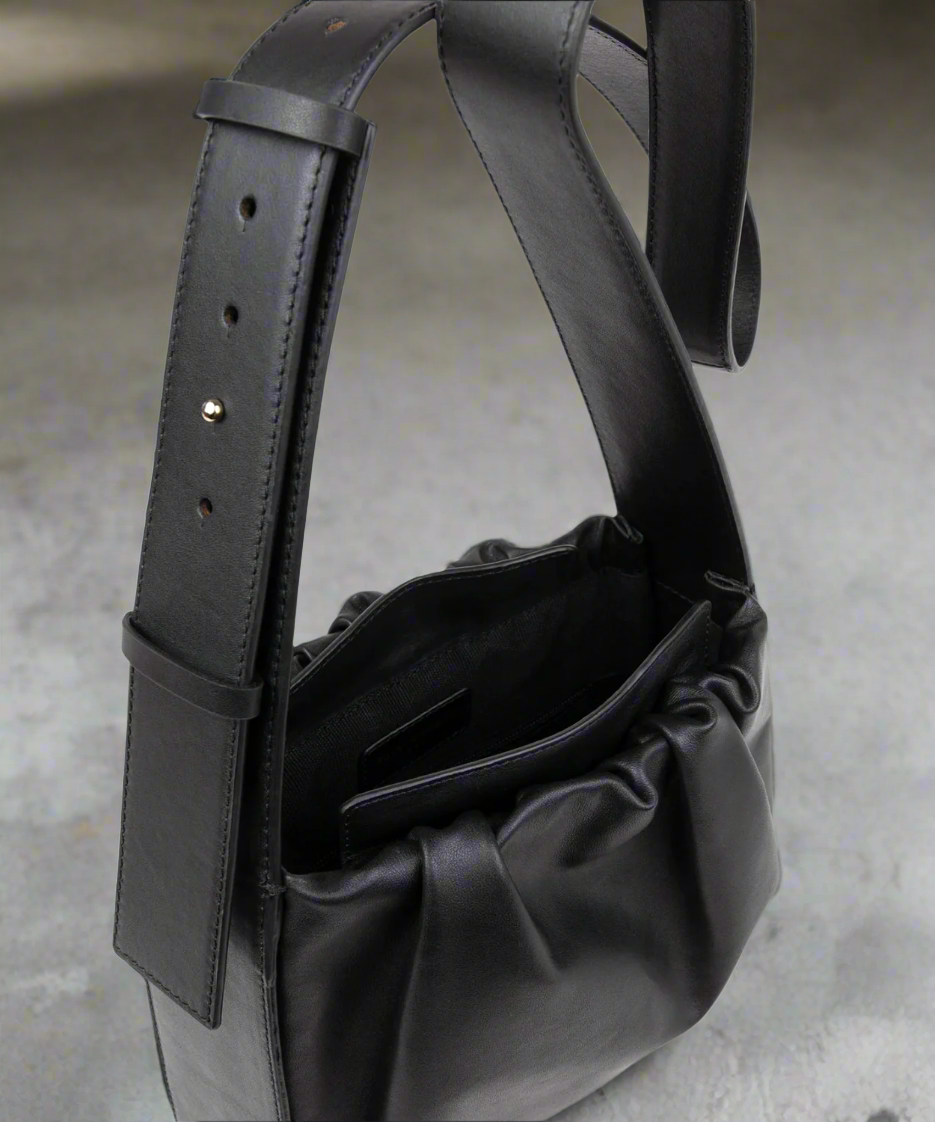 Black leather bag with a shoulder strap on a gray background