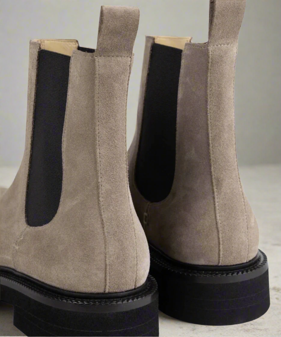 Pair of brown suede Chelsea boots with black soles on a gray background