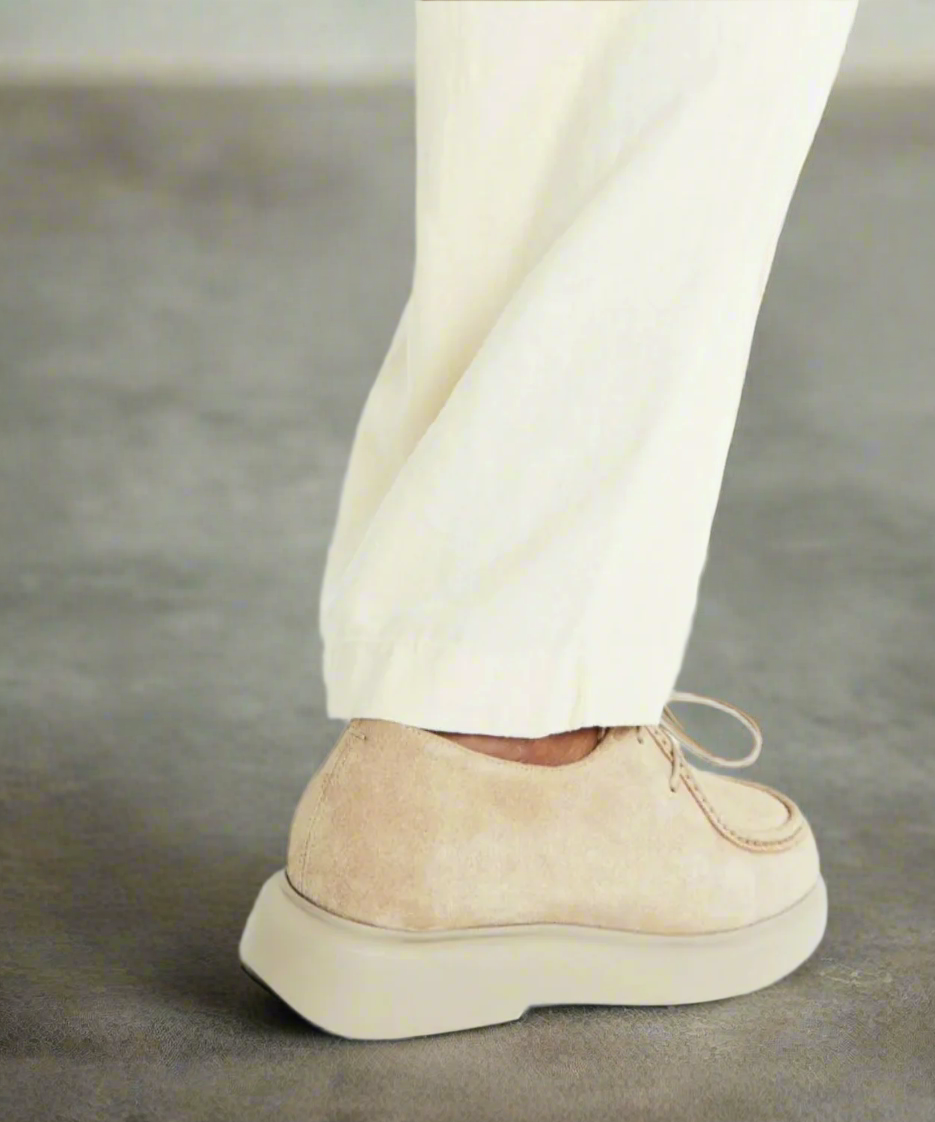 Beige suede loafer worn with cream pants on a gray background