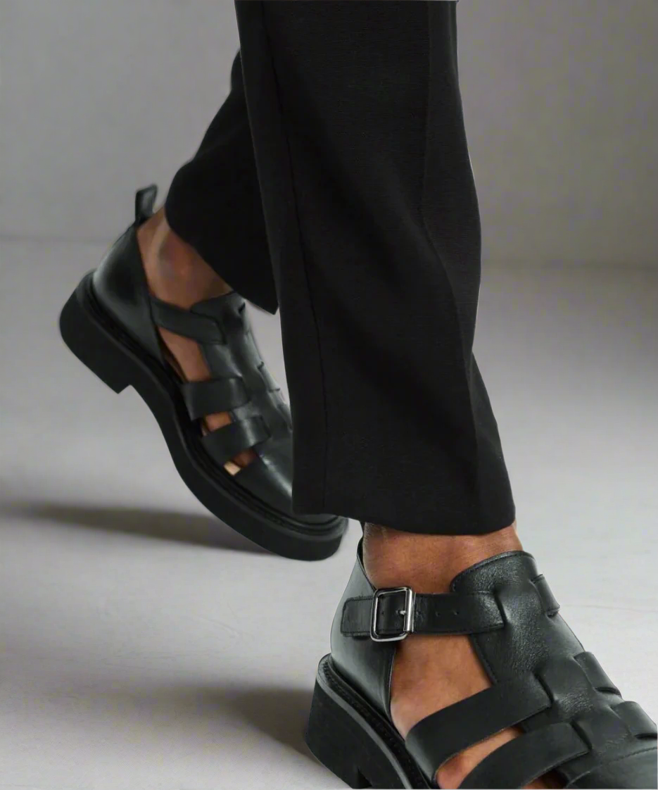 Black leather sandals worn with black pants on a gray background