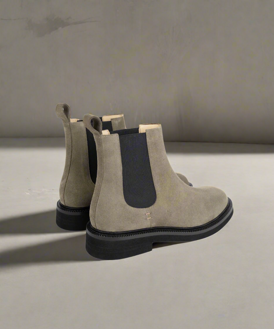 Pair of gray suede Chelsea boots with black elastic sides on a white background