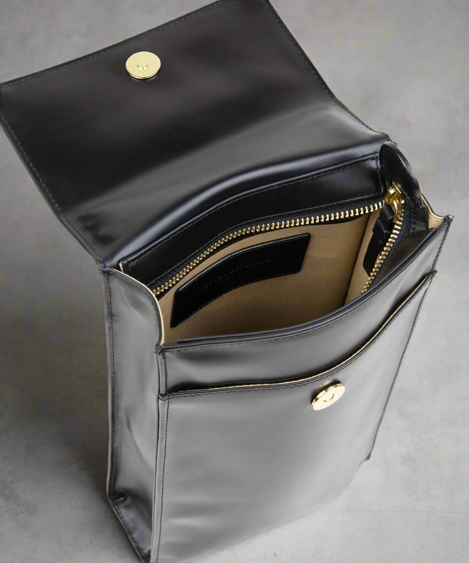 Black leather handbag with gold zipper and hardware on a light gray background