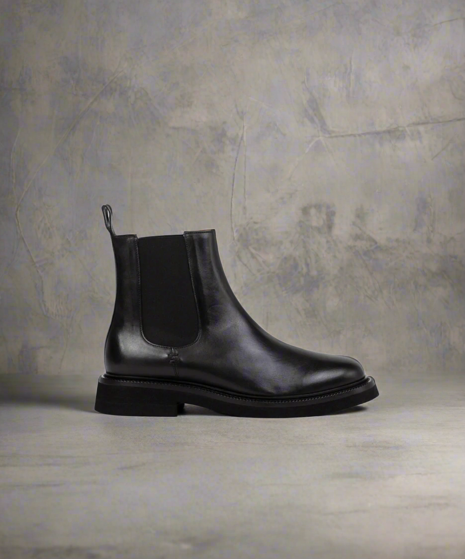 Black leather Chelsea boot on a textured gray background