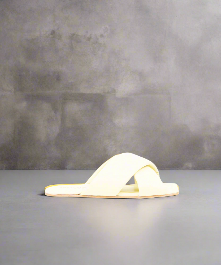 A light yellow flat heel sandal with a padded leather strap and cow leather lining, on a grey background.