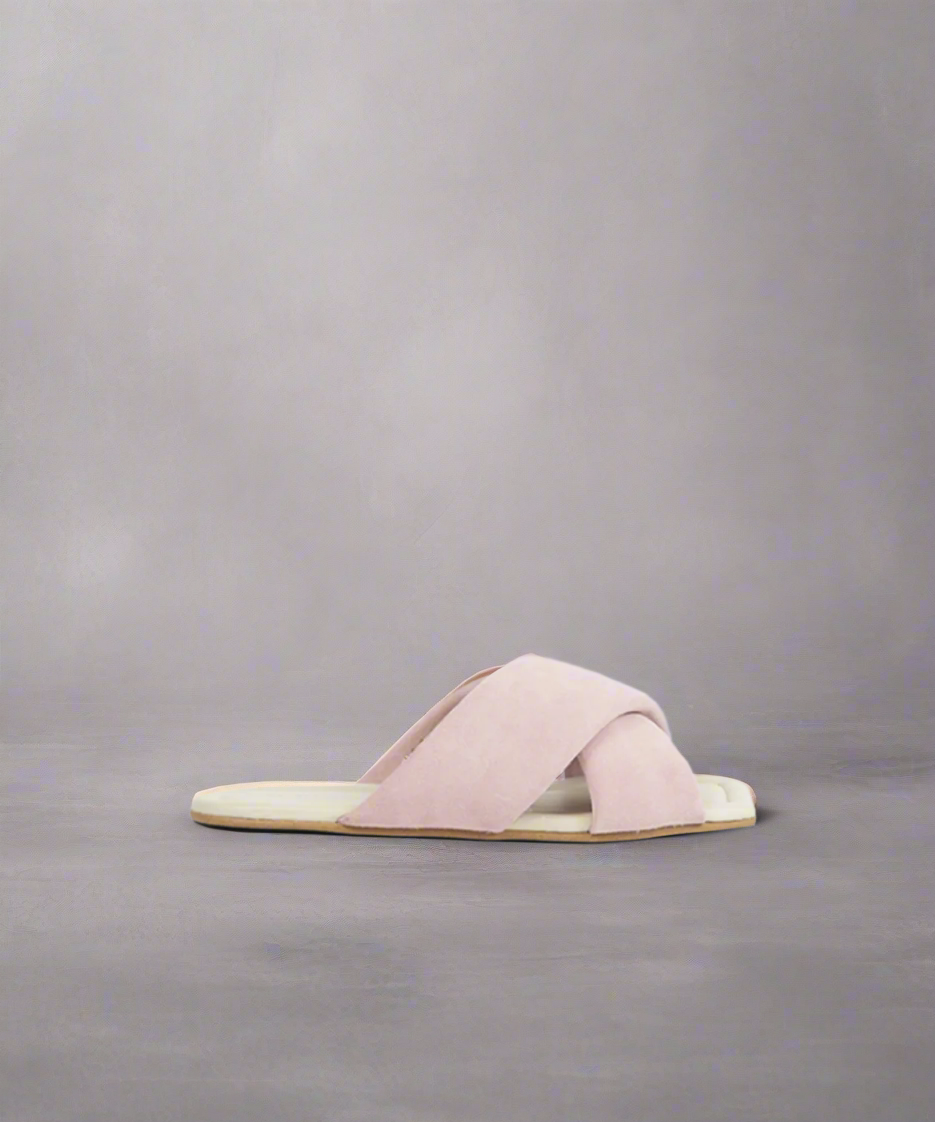 A light purple suede sandal with a flat heel and a curved toe line, displayed against a grey background.