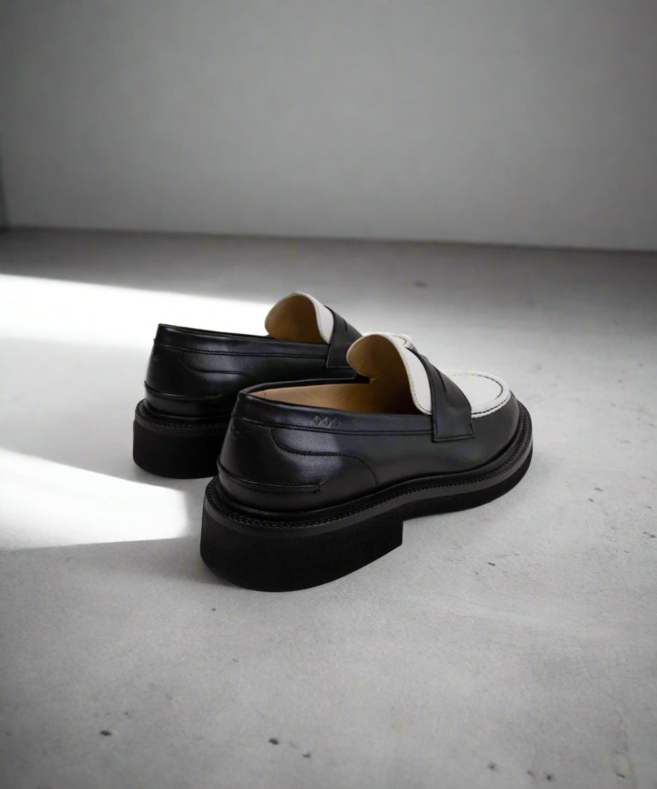 Black and white Royal RepubliQ loafers with white soles on a gray surface
