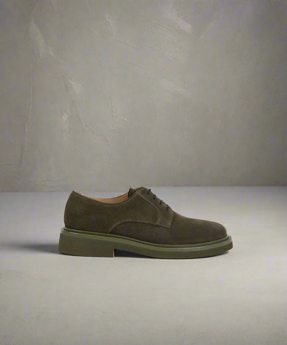 A dark khaki suede derby shoe with a green sole.