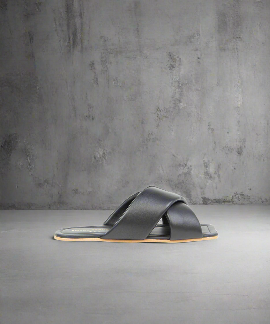 A black flat sandal with a smooth curved toe line and padded leather strap, handcrafted in Portugal.