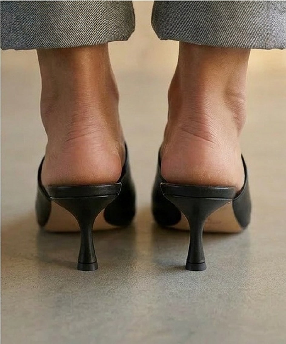 Black kitten-heeled shoes worn with gray pants on a neutral background