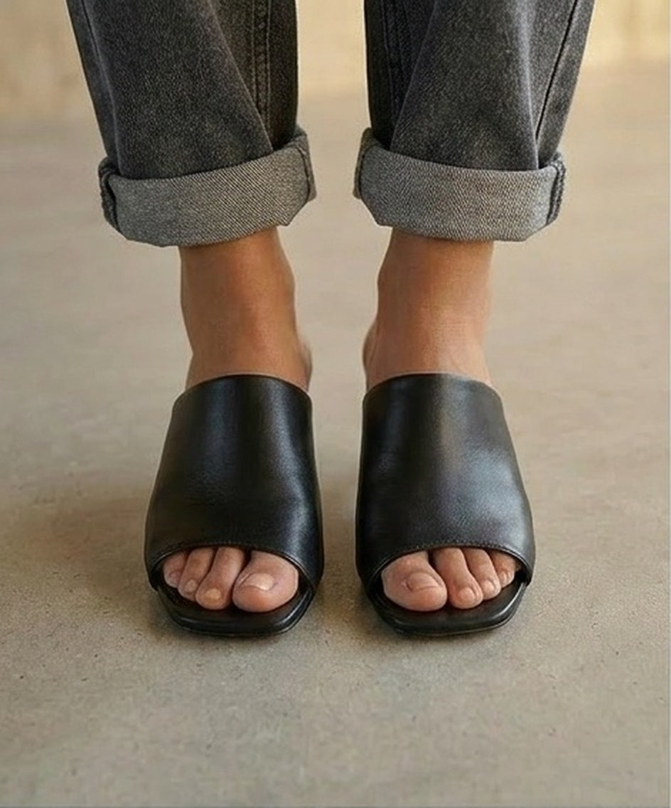 Black open-toe kitten-heel sandals worn with rolled-up jeans on a neutral background