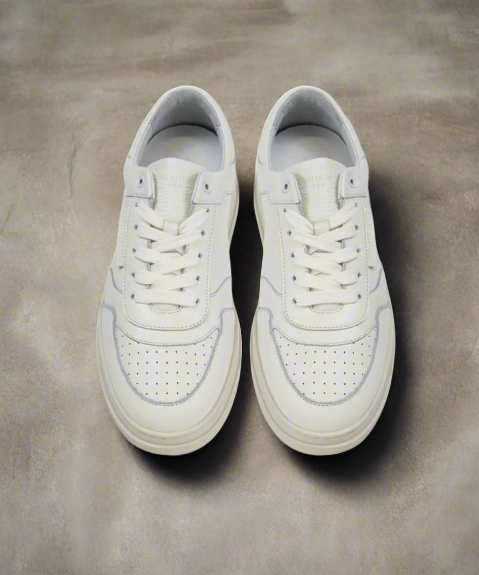 Pair of white Royal RepubliQ sneakers on a concrete surface