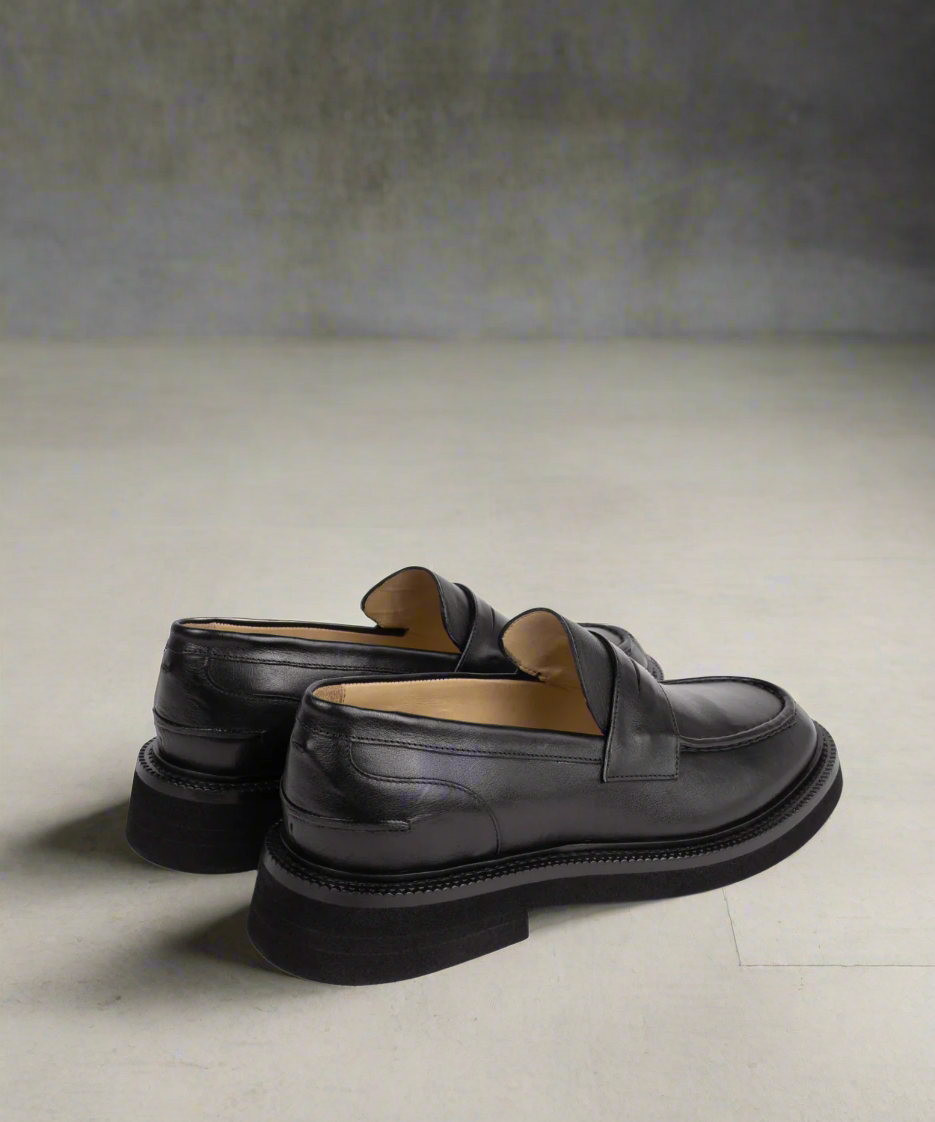 Pair of black leather loafers on a light gray background