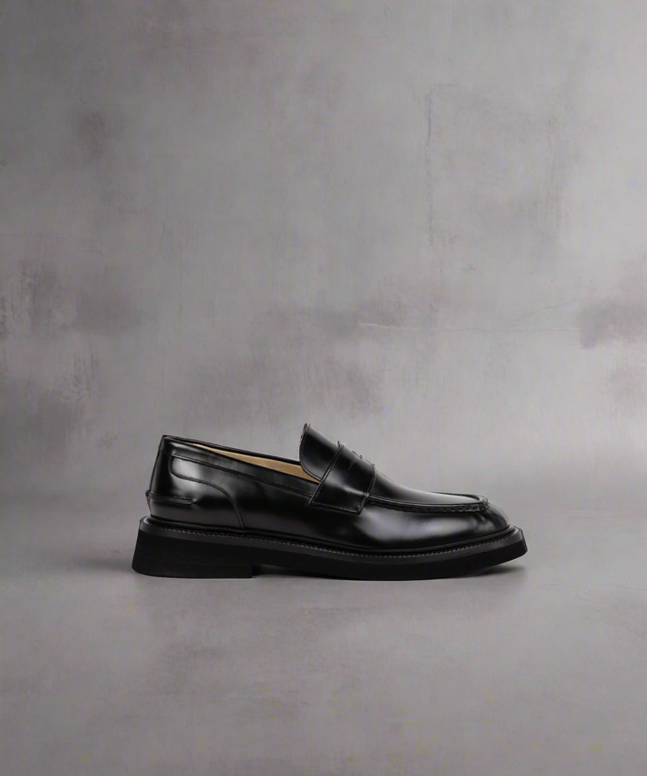 Pair of Royal RepubliQ black loafers on a gray surface with a neutral background