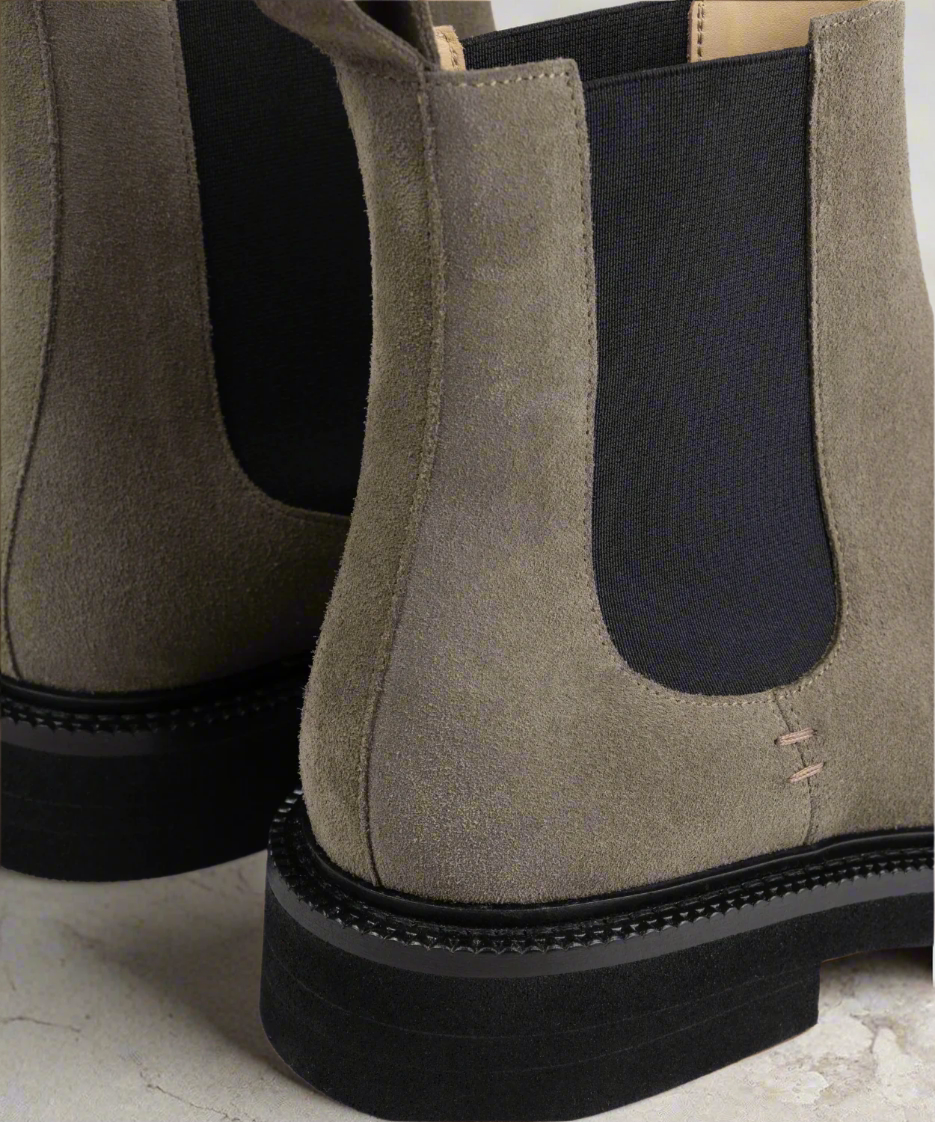 Close-up of a pair of brown Royal RepubliQ suede chelsea boots with black soles on a white background