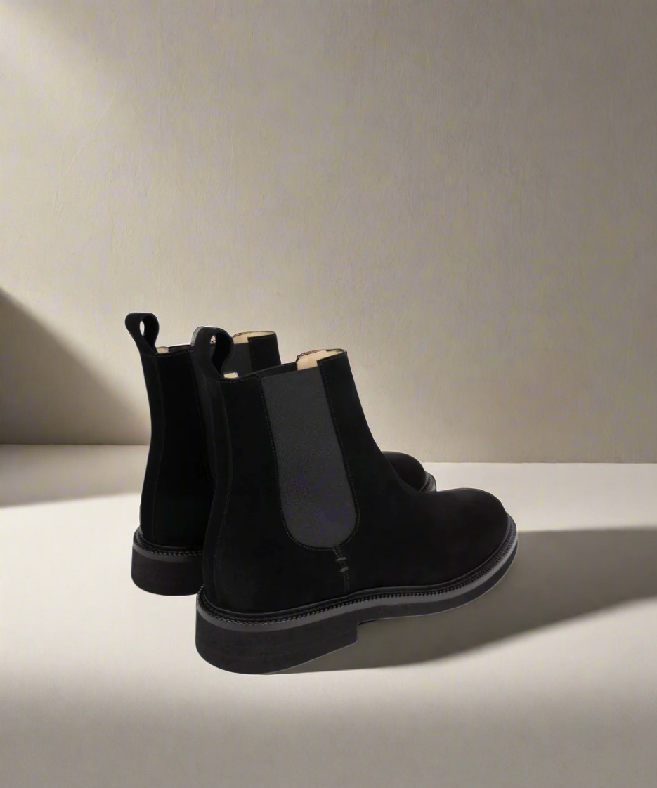 Pair of black Chelsea boots on a light surface with a neutral background