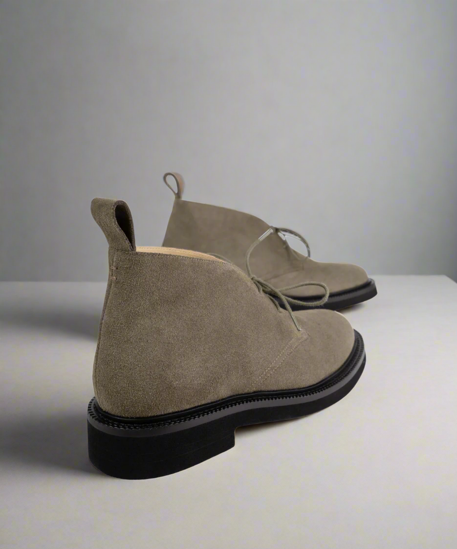Pair of beige Royal RepubliQ suede boots with black soles on a light gray background