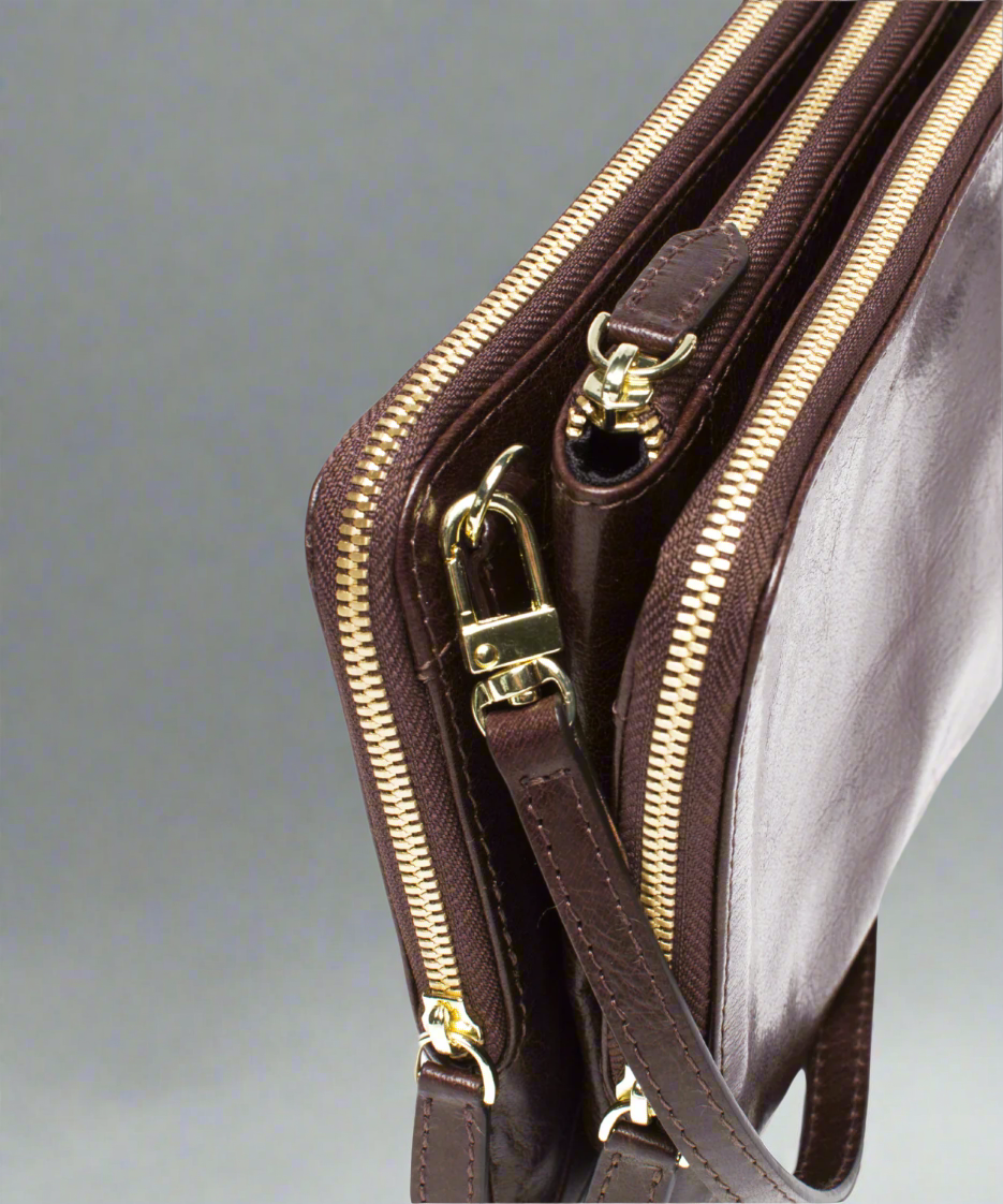 Close up of a Brown Royal RepubliQ leather clutch bag with a strap on a gray background