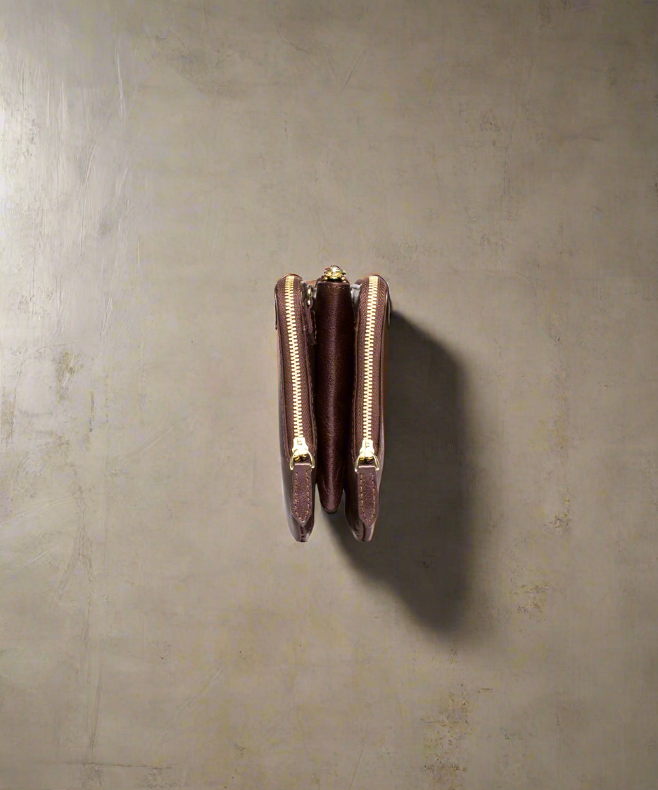 Side view of a Brown Royal RepubliQ leather clutch bag with a strap on a gray background