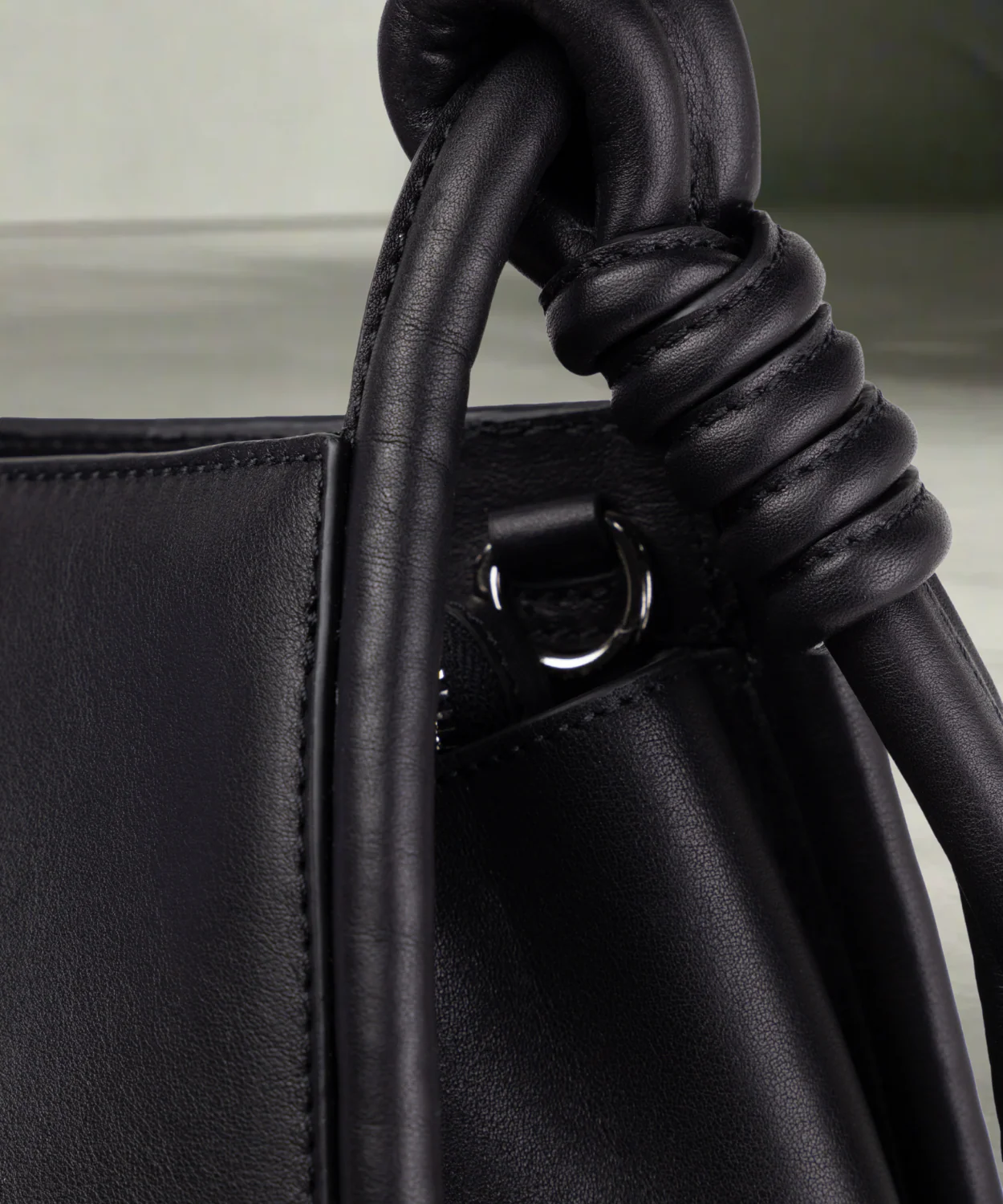 Close up of a black Royal RepubliQ leather shopper bag with a shoulder strap and a handle, displayed against a plain background.