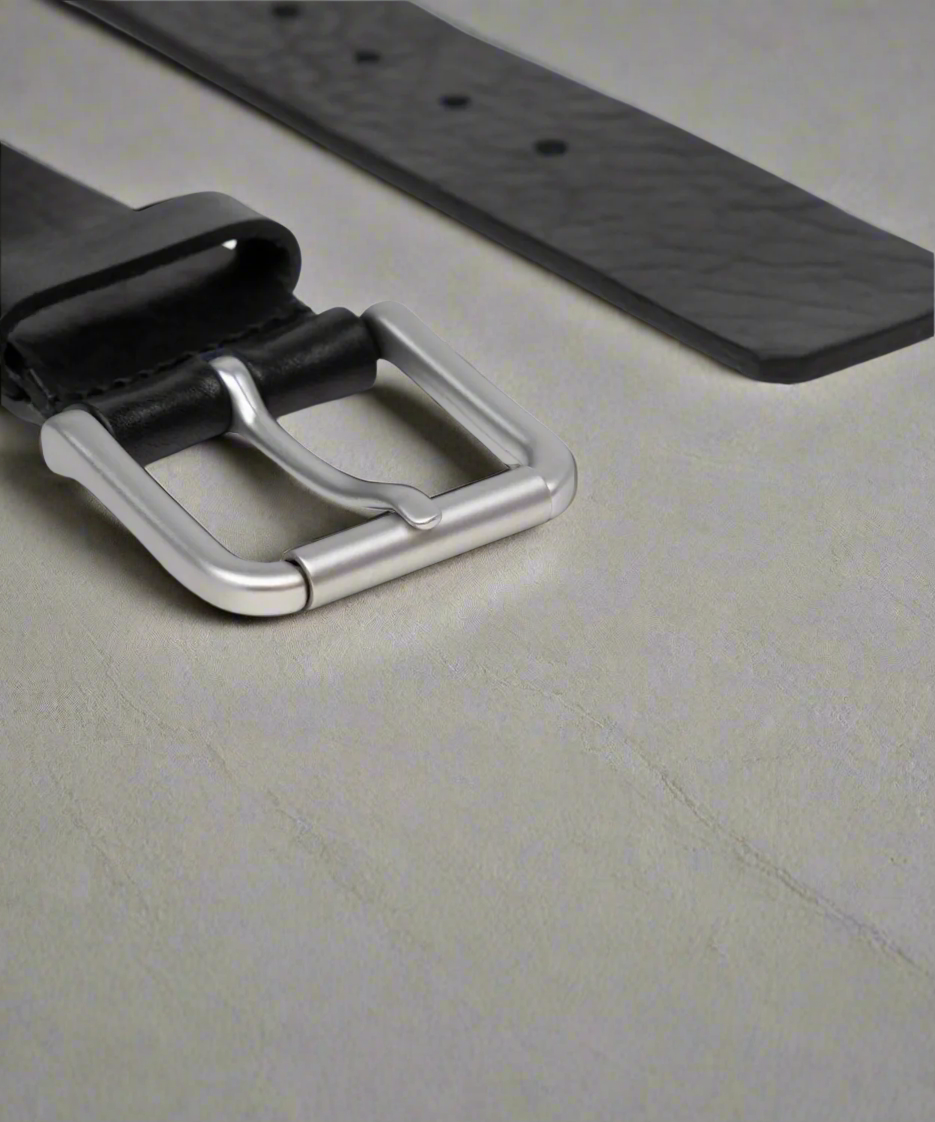 Close-up of a black Royal RepubliQ leather belt with a silver buckle on a light gray surface.