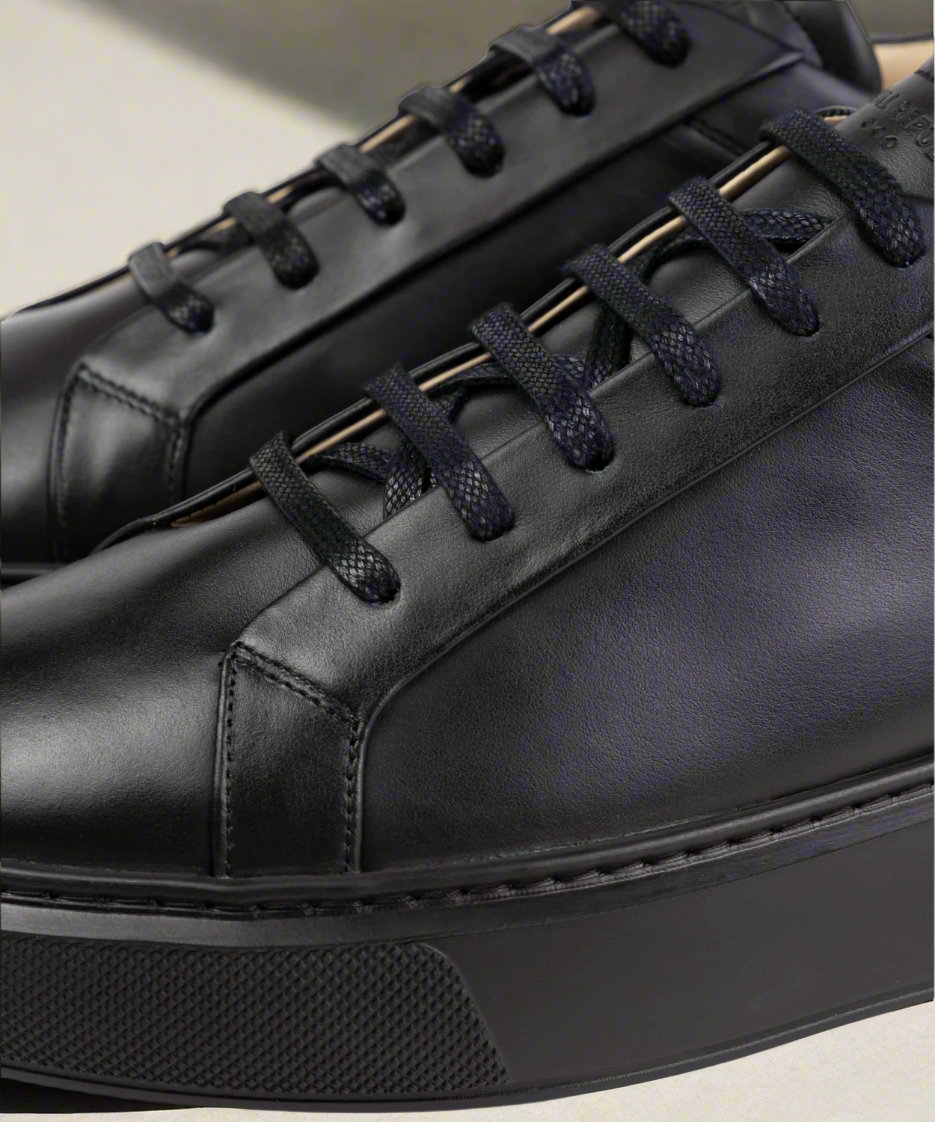 Close-up of black Royal RepubliQ leather shoes with dark laces on a light background