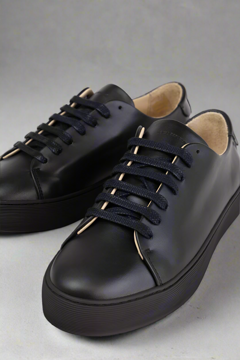 Close up of a Black Royal RepubliQ minimalistic leather sneaker on a gray background