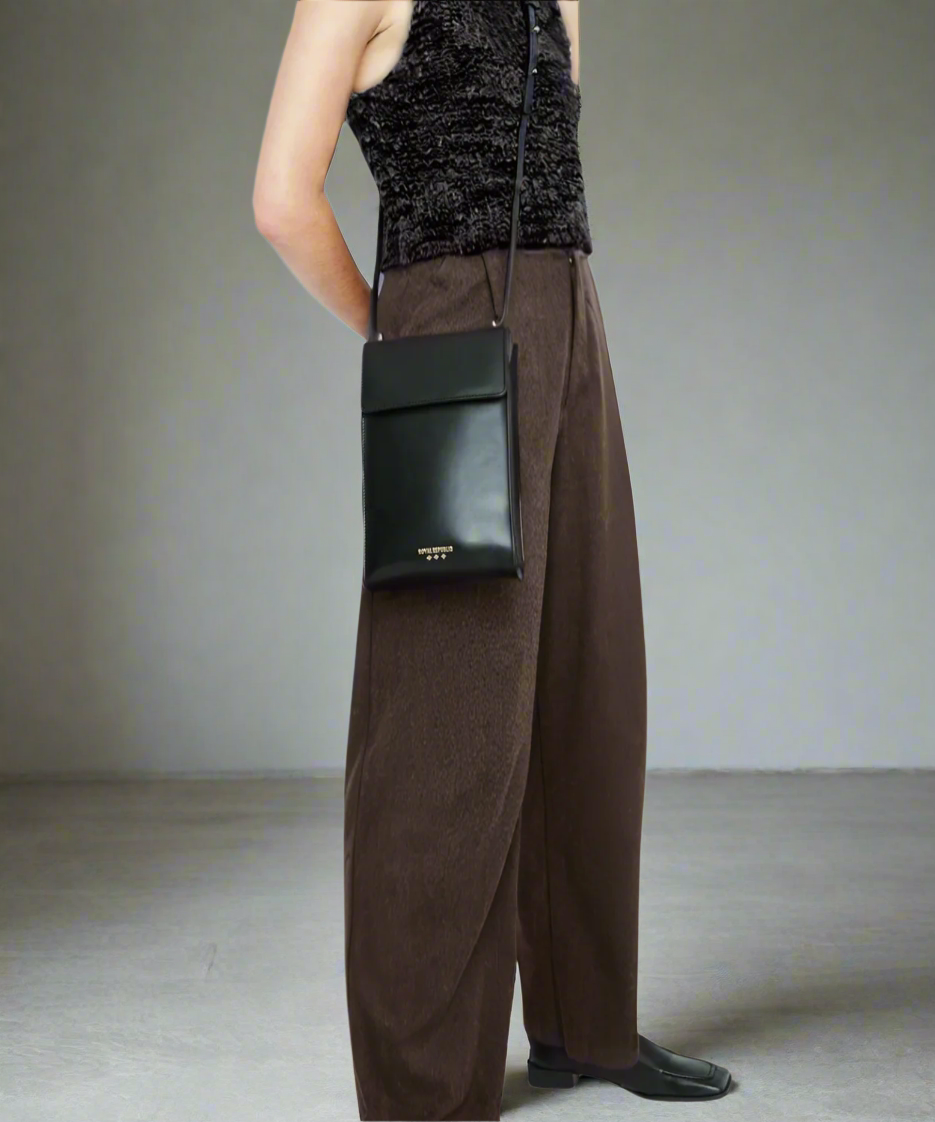 Person wearing a black sleeveless top and brown wide-leg pants with a black handbag on a gray background