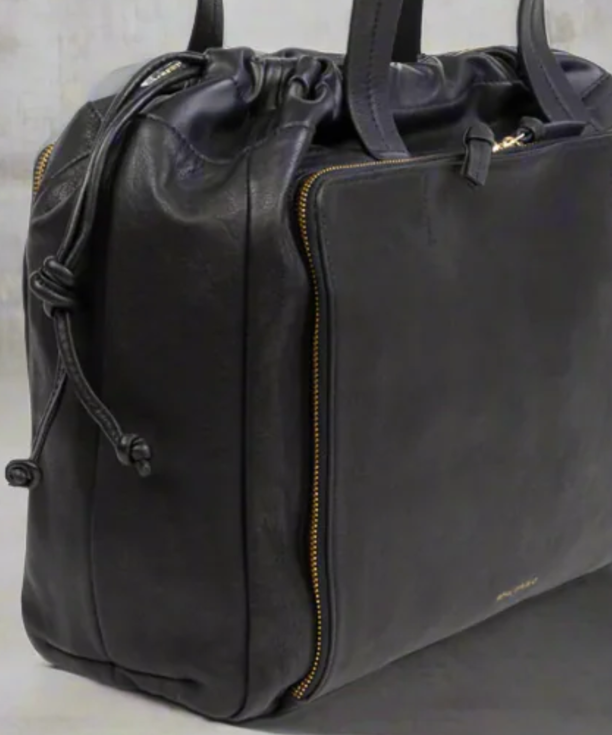 Black leather duffel bag with drawstring on a light gray background