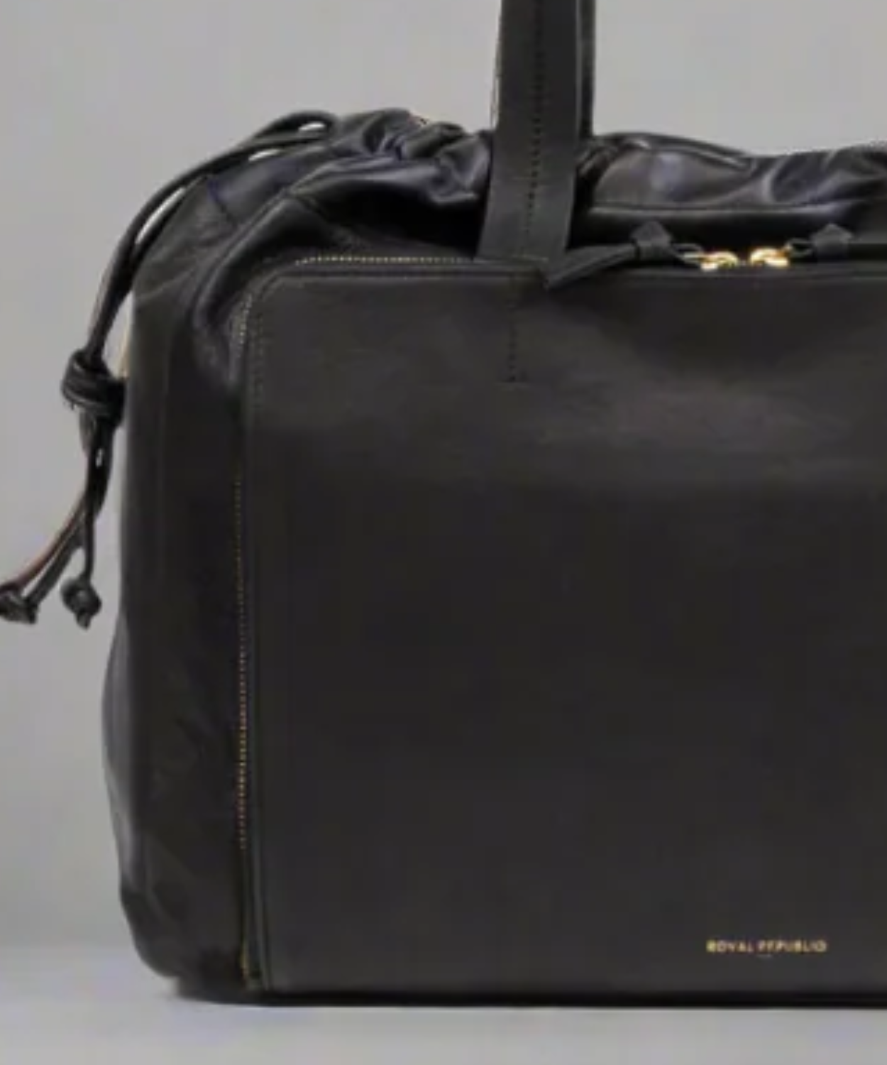 Black leather duffel bag with drawstring top on a light gray background