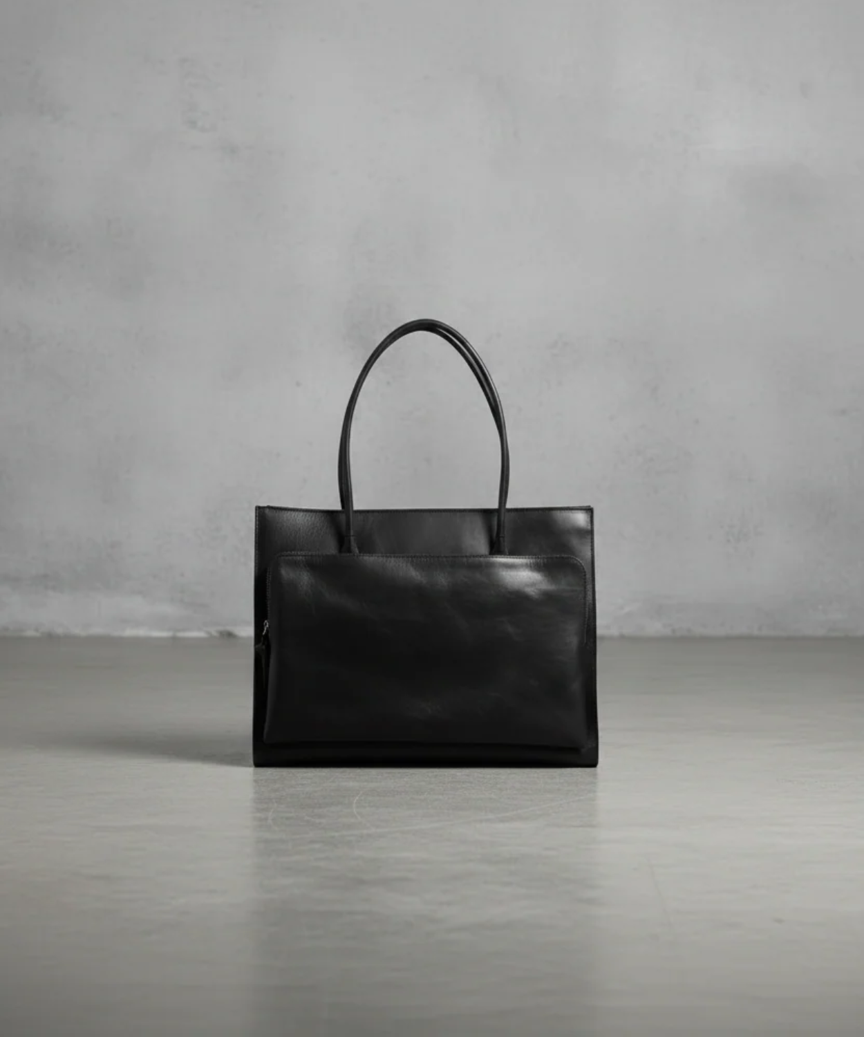 Black leather handbag on a gray surface with a gray concrete wall background