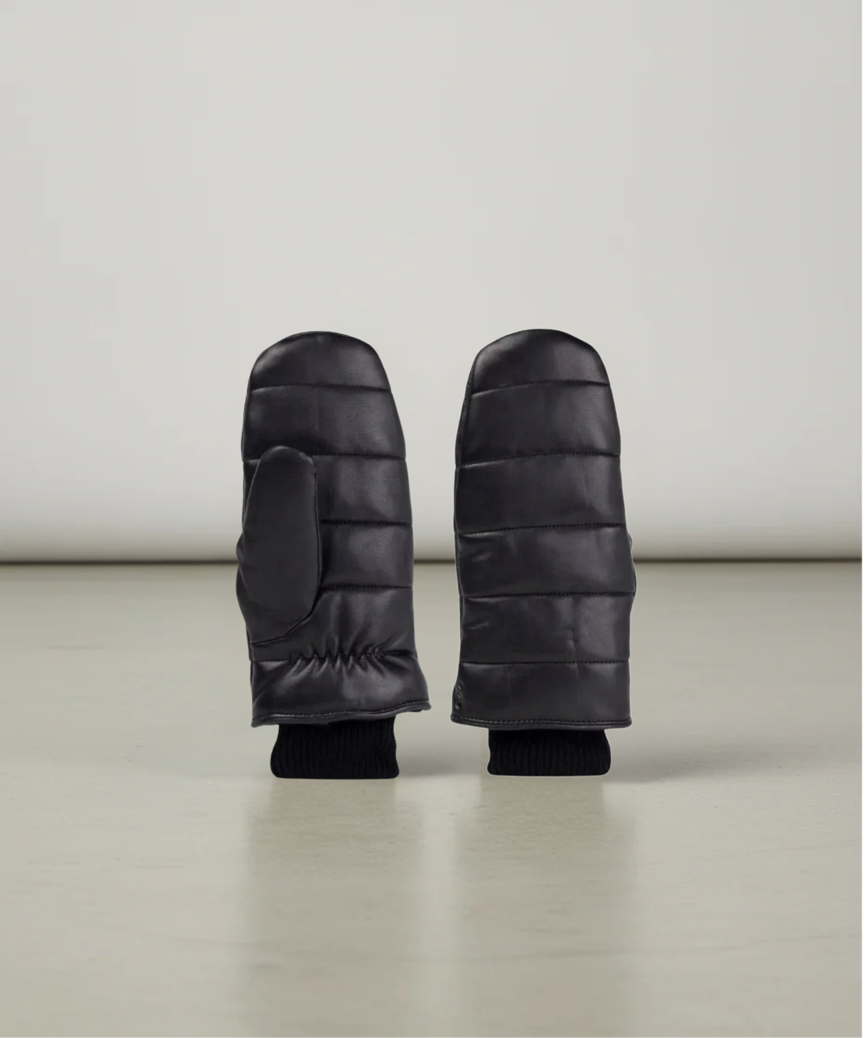 Pair of black puffer mittens on a light gray background