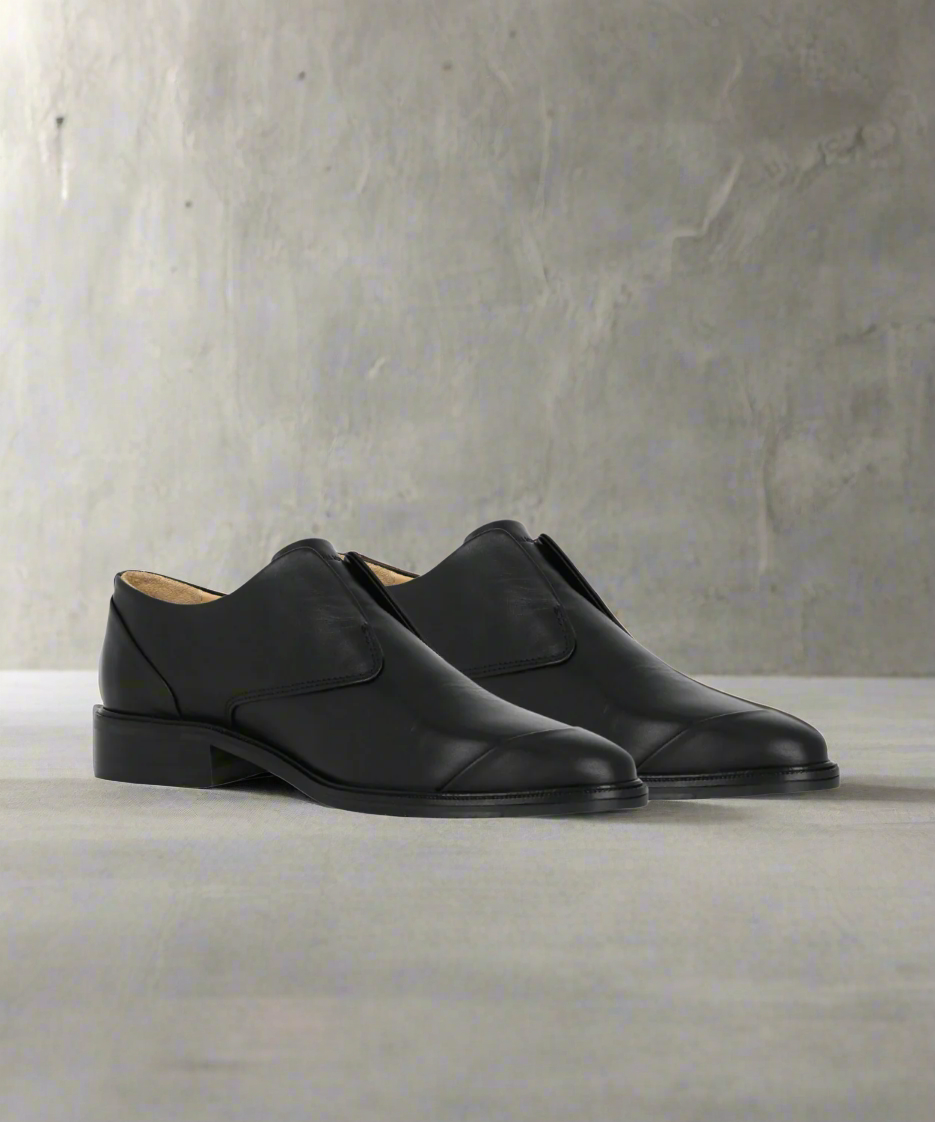 Pair of black Royal RepubliQ leather shoes on a light gray surface with a neutral background