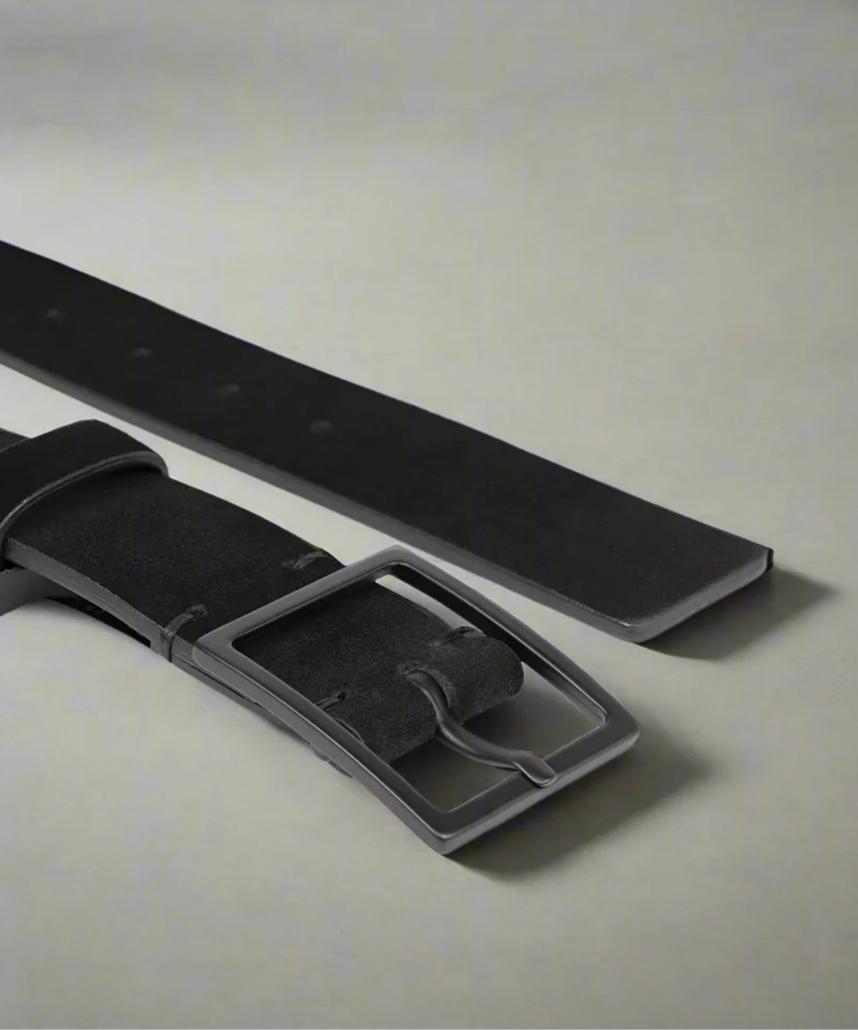 Black suede Royal RepubliQ belt on a textured beige surface with a light gray background