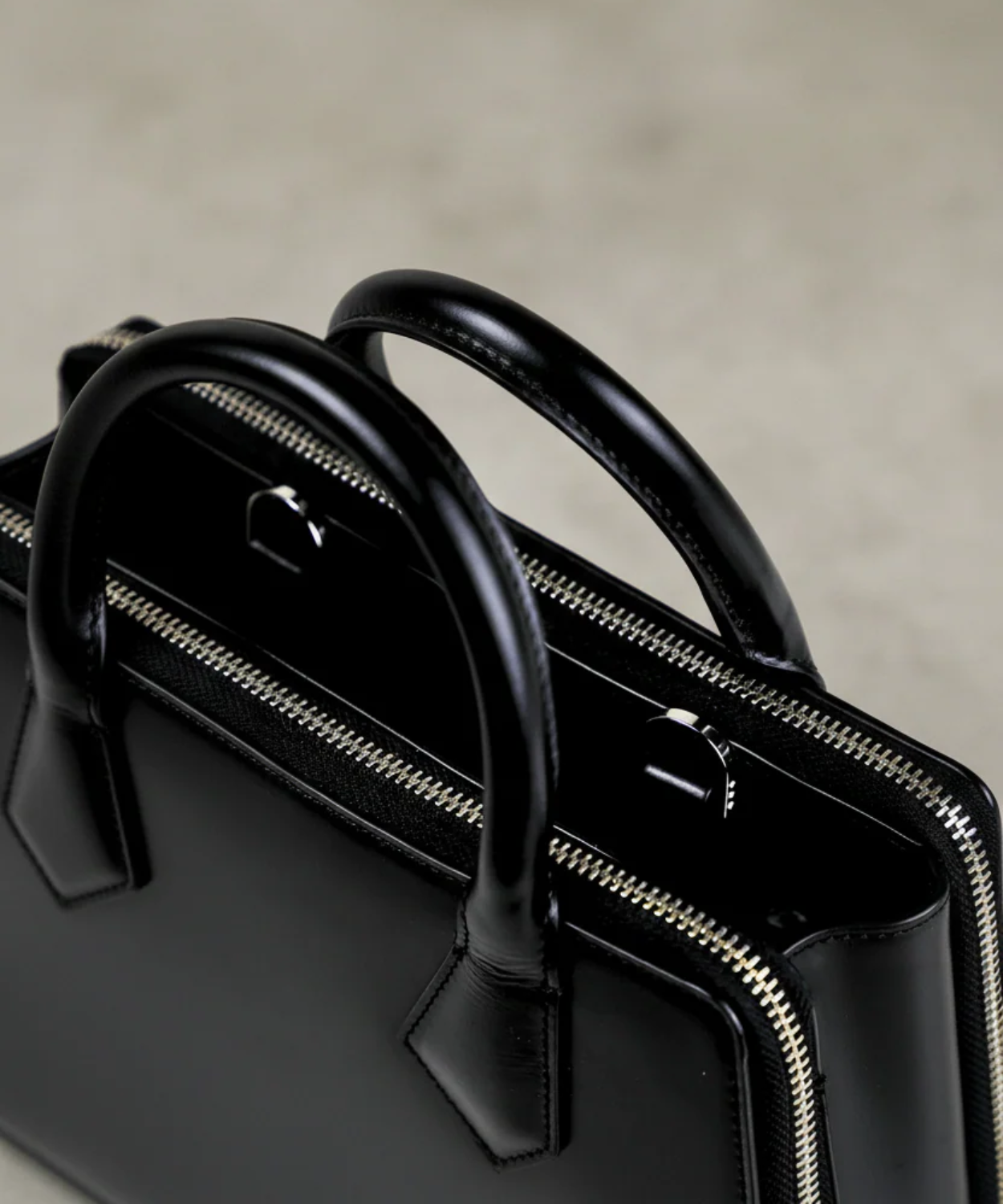 Black handbag with gold zipper on a neutral background