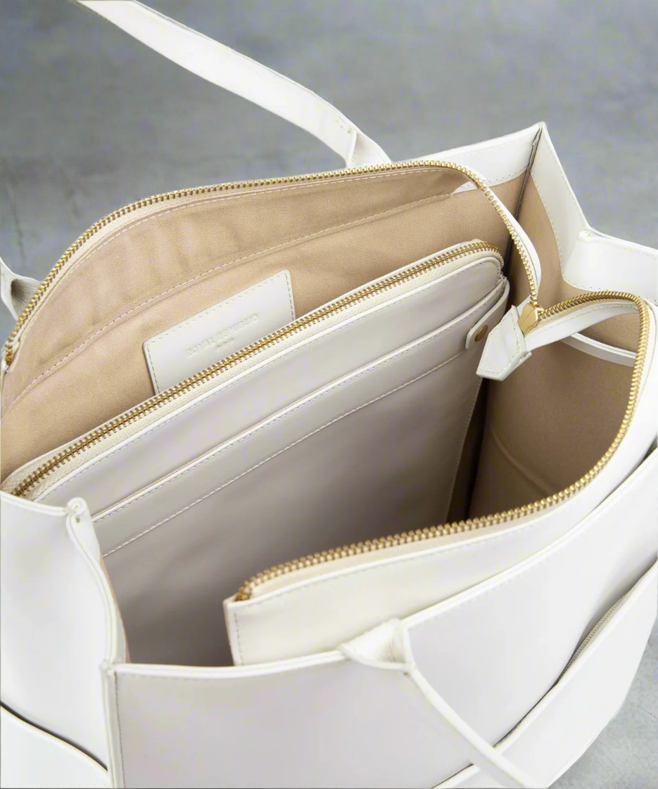 White handbag with gold zipper detail on a gray background