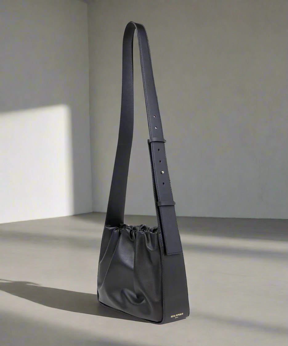 Black leather handbag with a strap on a gray background