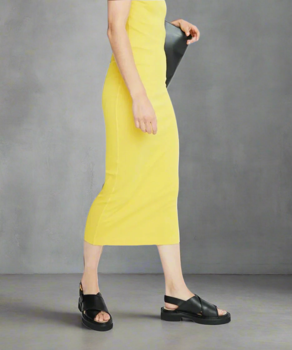 Person wearing a yellow dress and black sandals on a gray background
