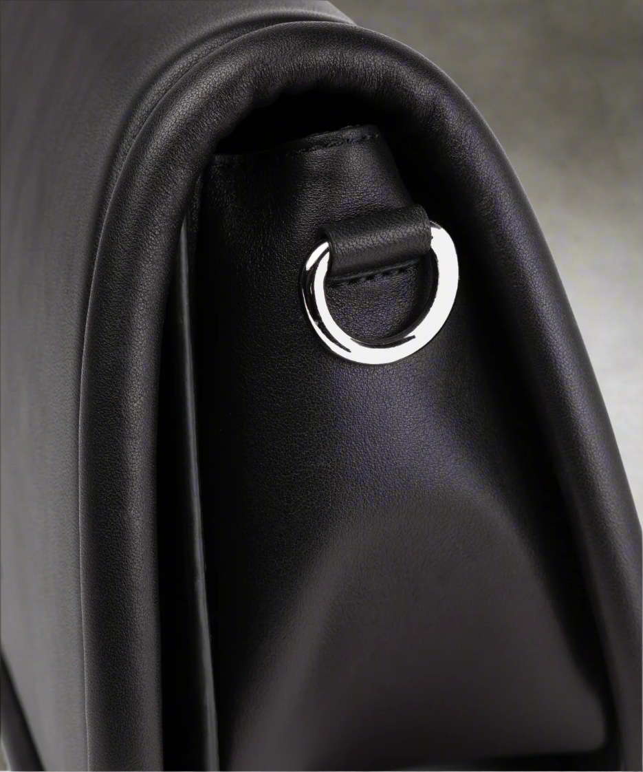 Close-up of a black leather bag with a silver ring detail on a gray background
